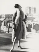 Modell i kappa med pälskant, klänning och hatt, på ett hustak. Kappa J. Heim, klänning original J. Patou.