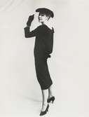 Modell i svart klänning med rosett baktill, pälshatt och handskar. NK:s Franska damskrädderi efter Balenciaga.