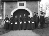 Konfirmandgrupp vid stigporten till Kungs-Husby kyrka, Uppland. Komminister Mats Åmark (1882-1973). Sannolikt den 2 maj 1914 (se historik).