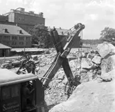 Wargöns AB. Byggnation av PM 5 1959-60. Foto och påförd  text av dåvarande ritkontorschefen Ragnar Söderberg.

 Grävskopans järnkäftar tuggar sig envist genom sprängstensmassorna.