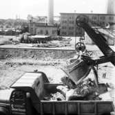 Wargöns AB. Byggnation av PM 5 1959-60. Foto och påförd  text av dåvarande ritkontorschefen Ragnar Söderberg.

 Grävskopan spyr ut sitt innehåll på de stora lastbilarnas flak.
