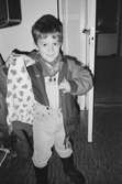 En pojke öppnar sin jacka och visar fordret på insidan som är tryckt med granar på ljus botten. Han står i entrén till Katrinebergs daghem, 1992.