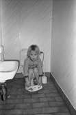 Ett barn som sitter på toaletten. På golvet ligger klinkers och till vänster syns ett handfat. Lille Skutt, Katrinebergs daghem, 1992.