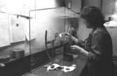 En kvinna i pappersfabriken mäter vikten på de olika skikten på den färdigtillverkade kartongen, 1980-tal. Bilden ingår i en serie från produktion och interiör på pappersindustrin Papyrus.