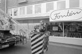 Uppsättning av blomlådor på hus vid Mölndals Torg med hjälp av kranbil, år 1985.

Fotografi taget av Harry Moum, HUM, Mölndals-Posten.