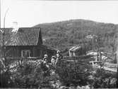 Kvinna med barn framför bostad i ett bergigt landskap.