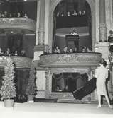 Modevisning på Stockholmsoperan, arrangerad av NK:s Franska damskrädderi. Mannekäng i dräkt från Balmain. På balkongerna sitter publik.