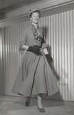 Modell i kort jacka och utställd kjol, knytblus, hatt och handskar. Från Dior.