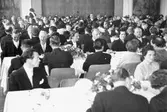 Flertalet människor som sitter vid uppdukade långbord i en stor lokal. 1940-tal.