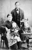 Porträttfoto av en stående man, en sittande kvinna (Edith Johansson) med ett litet barn i knäet samt en flicka som sitter på en egen stol. Edith arbetade i trädgården på Gunnebo slott 1914-1917.