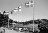 Vykort som visar de nordiska ländernas flaggor (förutom Islands) vid Stensjöns strandservering, 1970-tal. I bakgrunden Gunnebobro.