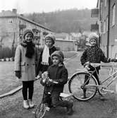 På gården vid Drottninggatan 18 i Huskvarna leker fyra flickor, en sitter på en trehjuling och en står vid en tvåhjulig cykel.
