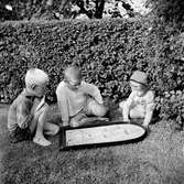 Tre barn, Tom Andersson till vänster, sitter i trädgården och spelar kulspelet Fortuna.