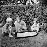 Tre barn, Tom Andersson till vänster, sitter i trädgården och spelar kulspelet Fortuna.
