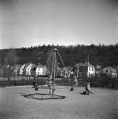 På lekplatsen i Mjölkafållan leker Tom Andersson, Kristina Wallsjö och Kenneth Wallsjö i en gungställning. I bakgrunden syns husen utmed Drottninggatan i Huskvarna.