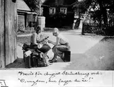 Fotografi av två unga damer sittande på resväskor. De håller en Musse Pigg figur mellan sig. I fonden Råbergska gården. Bildtext: Bevis för August Strindbergs ord: O ungdom, hur fager du är!