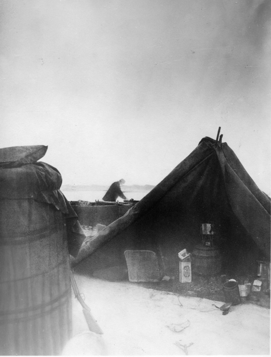 Nils Strindberg, Landningsplatsen. Troligen S A Andrée i bakgrunden vid båten. I förgrunden till vänster del av gondolen, till höger tältet med bland annat primus-köket. Retuscherad version av gm.III-59, dock monobild.