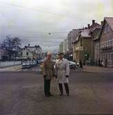 Lars och Lennart Tivelius står i korsningen Drottninggatan-Rosenborgsgatan i Huskvarna. Det är vinter och över Rosenborgsgatan hänger julstjärnorna uppe.