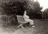 Nora Krantz (1879 - 1955) sitter på en bänk i trädgården, 1930- 40-tal. Troligtvis utanför deras hem (Stretereds personalbostad på Tulebovägen 23-27 i Stretered). Nora var gift med skomakaren Carl Krantz som undervisade på Stretereds skolhem.