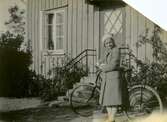 Rosa Krantz (1912 - 1994, gift Pettersson) står med sin cykel utanför föräldrarnas personalbostad på Tulebovägen 23-27 i Stretered, cirka 1932. Hon var dotter till skomakare Carl och Nora Krantz, båda anställda på Stretereds skolhem. Rosa gifte sig senare med skräddaren Bror Pettersson.
Originalfotot skadat efter en brand cirka 1945-1946 då makarna Pettersson hyrde en lägenhet i villa 