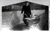 Rosa Pettersson (1912 - 1994, född Krantz) är ute på promenad med dottern Eva (född 1944, gift Kempe) som sitter i barnvagn, Stretered år 1945. 
Originalfotot är bränt och klippt efter en brand cirka 1945-1946 då makarna Pettersson hyrde en lägenhet i villa 