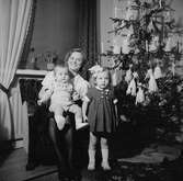 En mamma med två barn sitter bredvid en julgran som är klädd med pynt av silkespapper, glitter och levande ljus.