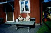 Maj-Britt Andreasson och Majken Olsson sitter på en bänk utanför Hembygdsgården Långåker 1:3 år 2000.