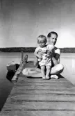 Bror Pettersson (1913 - 1984) och dottern Eva (född 1944, gift Kempe) befinner sig på en brygga vid Tulebosjön år 1945. Till vänster, utmed bryggan, ligger en fastsurrad eka.