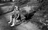 Eva Pettersson (född 1944, gift Kempe) sitter på sin trehjuling på en väg i Torrekulla, år 1948. Dotter till Bror och Rosa (född Krantz) Pettersson.