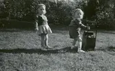 Syskonen Kjell (1945 - 1998) och Ann-Charlott Johansson leker med en dockvagn på en gräsmatta i Torrekulla år 1952. Barn till Allan och Margit Johansson. Allan arbetade som rättare vid flickhemmet i Torrekulla, där även Margit arbetade. De bodde i gamla huvudbyggnaden men byggde senare egen villa på Nyhagenvägen i Torrekulla. Relaterat motiv: A2355.