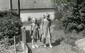 Systrarna Karin (född 1947, gift Hansson) och Eva Pettersson (född 1944, gift Kempe) promenerar med skolväskor vid Karins första skoldag, Gamlehagsvägen 17 i Torrekulla år 1954. Döttrar till Bror 