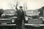 Fritiof (elev boende på Stretereds skolhem) iförd polisuniform, står mellan två taxibilar vid Kållered station, 1940-tal. Han fick 