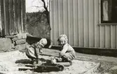 Kusinerna Stina Krantz och Eva Pettersson (född 1944, gift Kempe) leker i sandlådan vid Torrekulla gård cirka 1947. Stina är dotter till Edit och Östen Krantz, Eva är dotter till Bror och Rosa Pettersson (född Krantz) i Torrekulla.