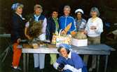 Lindberedningsgruppen från Kållered Hembygdsgille är på besök vid Långåker, 1980-tal. Från vänster: 1. Sibyl Berzins, 2. Stina Svensson, 3. Helky Arndtsson, 4. Maj-Britt Andersson, 5. Dagmar Svensson, 6. Emy Johansson. På huk framför bordet: Berit Thalenius.