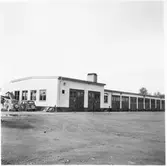 Vägstation C1, Enköping. Huvudbyggnad, med från vänster; verkstadsdel, kontorsdel, garagedel. Personbilar parkerade vid gaveln.