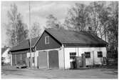 Vägstation C5, Rasbo. Filial Skoby. Garagebyggnad invid väg. Bensinpumpar (drivmedelspumpar). Radiomast. Personbil framför garaget. Bakom garaget vägmärke (orienteringstavla) liggande på marken. Text bland annat 