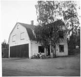 Vägstation D1, Närsjö. Bostadshus med garage vid gaveln. Flicka vid cykel.