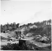 Vägstation D2, Kjula. Grusgropen norr om vägstationen. Vägstationens huvudbyggnad i bakgrunden. Asfaltverk. På kanten av grusgropen tankvagn, märkt 