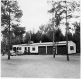 Vägstation D4, Katrineholm. Vägstationens huvudbyggnad med verkstads-, kontors- och garagedel. Personbilar framför byggnaden.