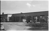 Vägstation D5, Flen. Huvudbyggnaden med Depåverkstaden till höger. Framför verkstadsdörrarna en Volvo Duett, stenkross och lastbil (utan flak).