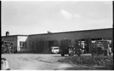 Vägstation D5, Flen. Huvudbyggnaden med Depåverkstaden till höger. Framför verkstadsdörrarna en Volvo Duett, stenkross och lastbil (utan flak).