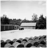 Vägstation E6, Mantorp. Garagebyggnad, förrådsbyggnad. På garageplan en lastbil. Bränslefat i förgrunden.