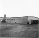 Vägstation E8, Ringarum. Byggnad med verkstadsdel, kontorsdel och garagedel. Personbilar parkerade framför garageport. Stående bränsletank vid gaveln.