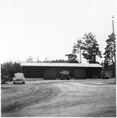 Vägstation E10, Östra Husby. Garage- och förrådsbyggnad. Personbil, E10304, framför byggnaden. Luttunna på vagn, plogar till vänster.