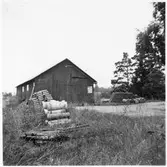 Vägstation E10, Östra Husby, filial Kummelby. Garagebyggnad med port på gaveln. Upplag av täckdikningsrör, bränslefat, märkta 