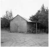 Vägstation E11, Motala, filial Berg. Garage- eller förrådsbyggnad i korrugerad plåt. Port på gaveln. Cykelställ med cyklar.