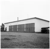 Vägstation E12, Tjällmo. Garagebyggnad, mansperson. Cykelställ med cyklar vid gaveln.