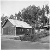 Vägstation E13, Stjärnvik, filial Kimstad. Garagebyggnad med portar på gaveln. Diverse materialupplag i bakgrunden. Invid väg med busshållplatsmärke 