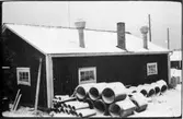 Vägstation F4, Bredaryd. Förråds- eller garagebyggnad, baksida. Upplag av cementrör.