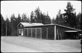 Vägstation F13, Hjältevad. Förråds- och garagebyggnad, invid väg. I vinkeln mot garagelängan en byggnad, eventuellt kontorsdel. Cykelställ med cyklar vid gaveln.